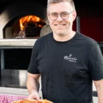 Portret van pizzabakker met verse pizza voor houtoven tijdens zakelijke brandingshoot Il Rimorchio