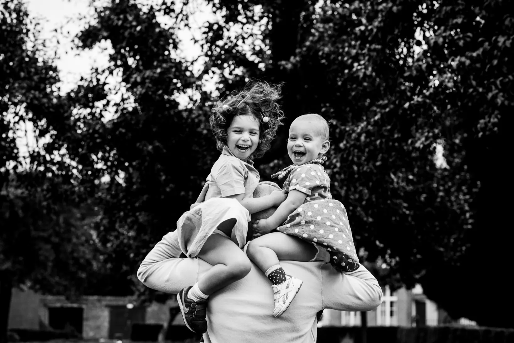 Zwarte-wit familiefoto van vrolijke meisjes op de schouders van hun papa tijdens een speelse fotosessie