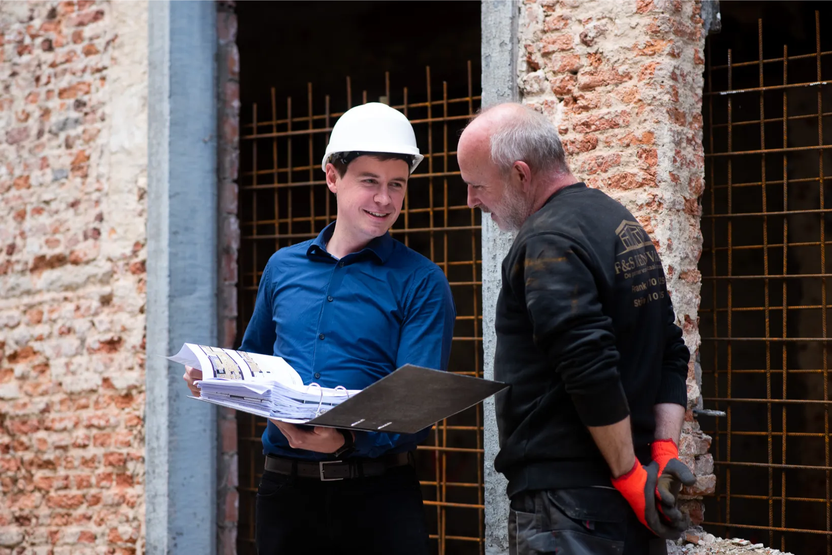 Projectleider en bouwvakker bespreken plannen op bouwwerf met zichtbare bakstenen muur