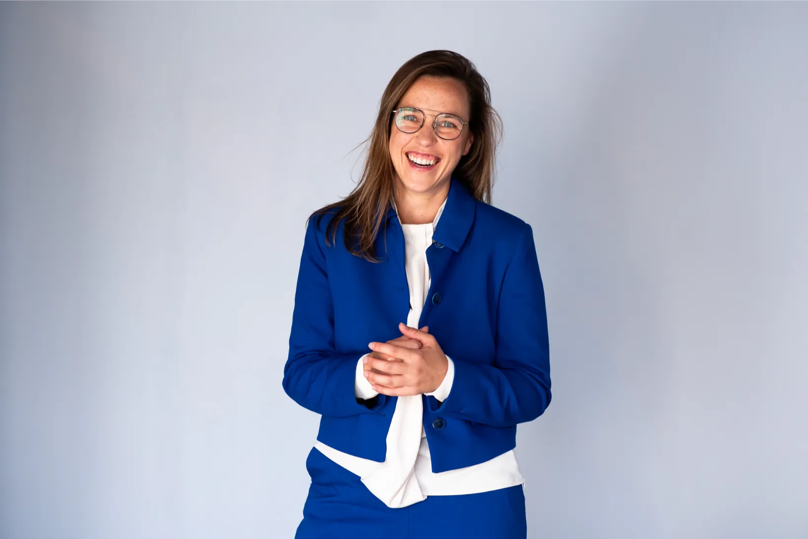 Professionele portretfoto van een vrouw in blauwe blazer, spontaan en warm gelachen voor een neutrale achtergrond.