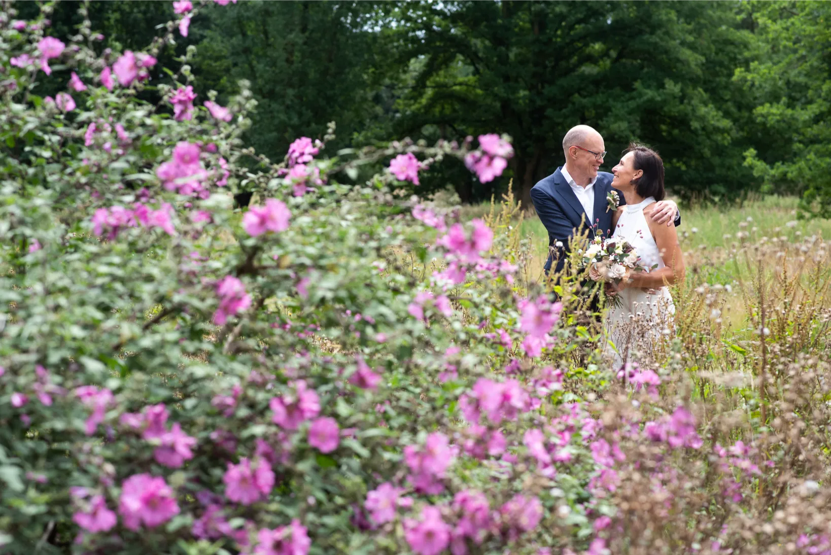 Tussen bloemen en zonlicht deelt een bruidspaar een spontaan moment in een zomers veld.