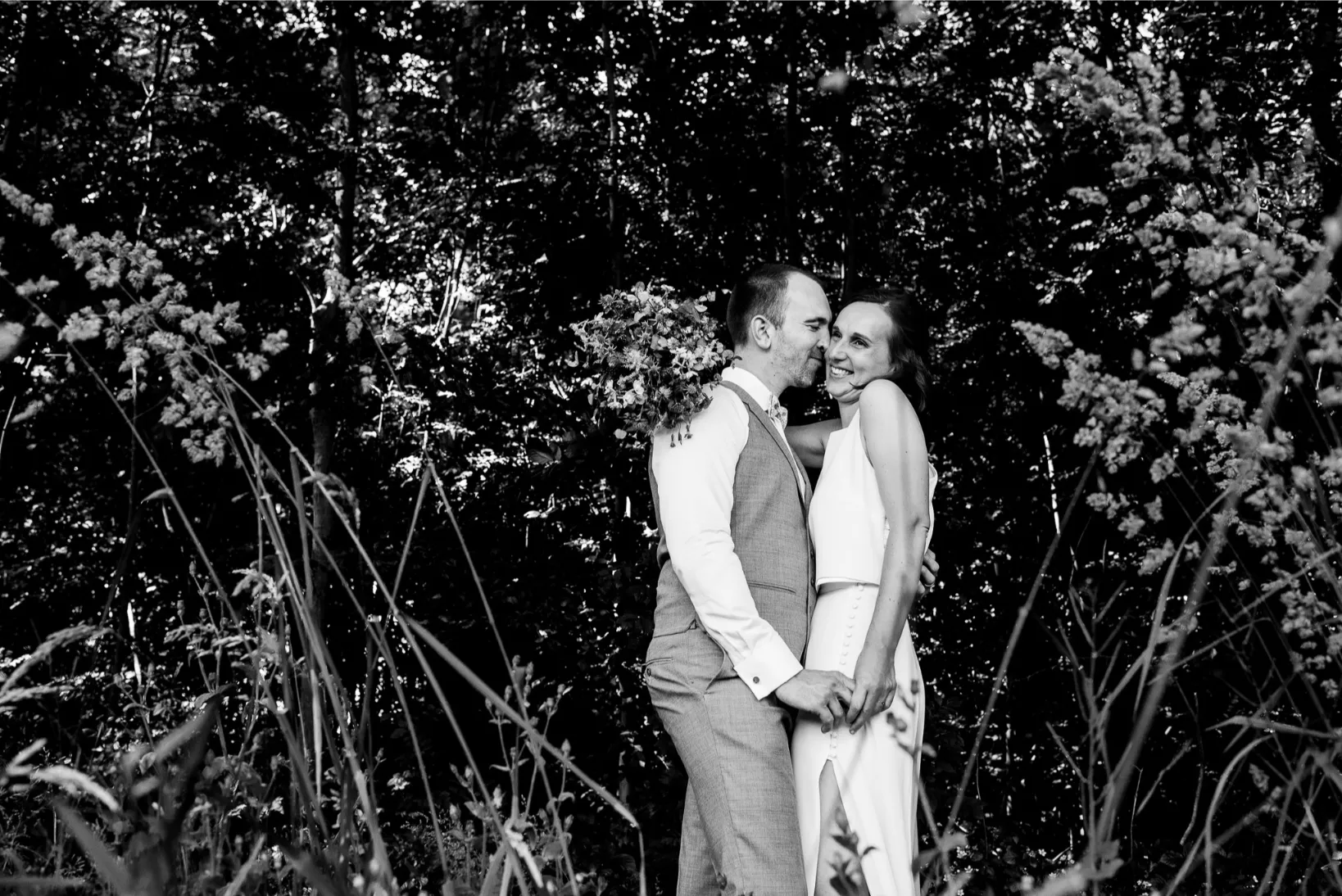 Zwart-wit beeld van een intiem trouwmoment in het bos — ongedwongen en liefdevol.
