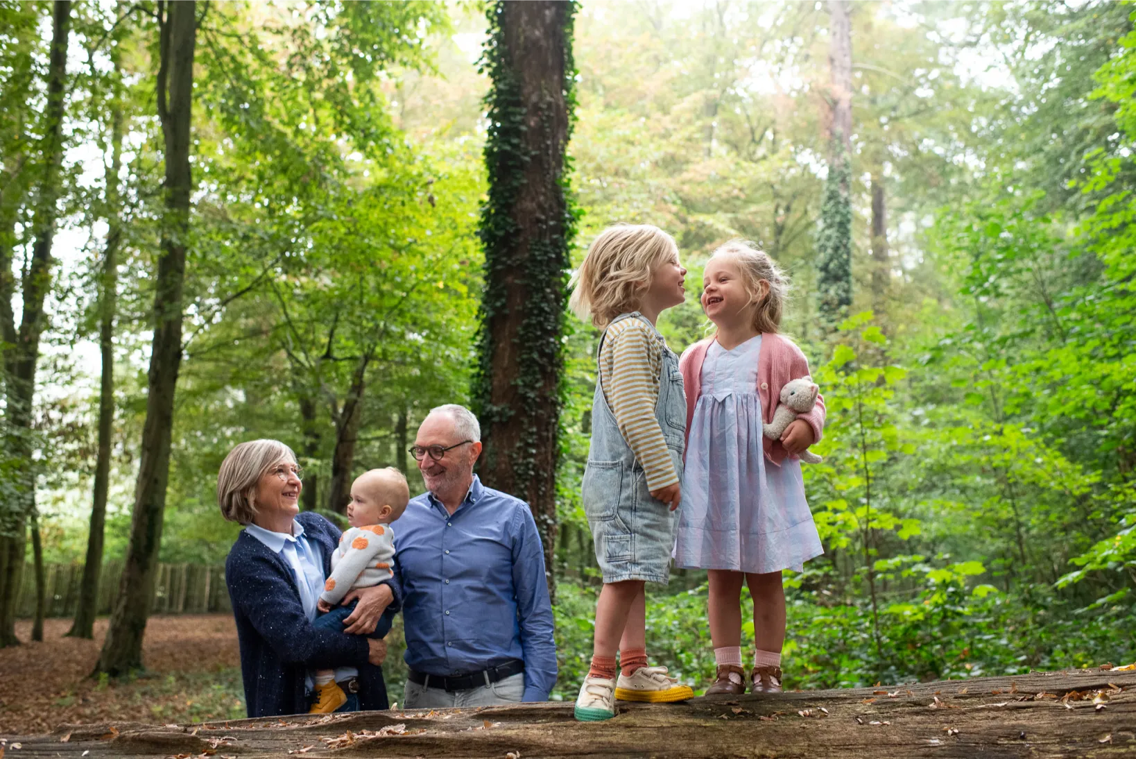 Oma en opa met kleinkinderen tijdens speelse familiefotografie in het bos – ontspannen moment in de natuur.